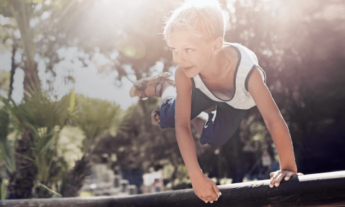 Boy jumps over an ostacle in playground. Sun is shining.