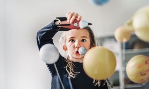 A kid plays with toy rocket ship, planets in the foreground